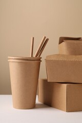 Wall Mural - Eco friendly food packaging. Paper containers and straws on white table against beige background