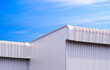 Geometric metal industrial warehouse building with 2 aluminium roof eaves against blue sky background, low angle and perspective side view with copy space 