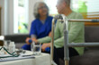 Select focus on metal walking frame against blurred doctor consulting elderly patient in a nursing home