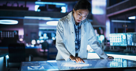 Female Asian Neuroscinetist Using Interactive Touch Screen Table With MRI Scans On Display In Modern Biotechnology Research Center. Doctor Developing Innovative Devices For People With Brain Damage.