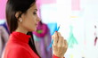 Focus on female hand holding blue pencil. Lady in fashionable red blouse standing at workplace and looking at something with interest. Pretty designer creating new project. Blurred background