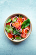 Salad with tomato, fresh leaves, and onions, overhead flat lay shot. Healthy diet, simple vegan recipe, on a slate background