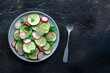 Fresh cucumber and radish salad with parsley, overhead flat lay shot. Simple vegan recipe on a black stone background. Healthy diet, with copy space