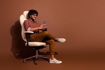 Sticker - Full size photo of nice young man sit chair smart phone empty space wear shirt isolated on brown color background