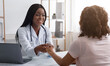 Cheerful female doctor holding patient hand, clinic interior