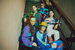 Vibrant youth atmosphere. Young boys and girls, friends wearing colorful 90s style sportswear, posing on stairs, entryway. Concept of 90s, fashion, youth culture, old-style trends