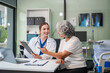 © NanSan - Monthly health check-ups and counseling sessions are provided to an elderly Asian woman by a Caucasian female caregiver, offering support, advice, and motivation.