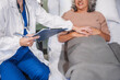 © NanSan - Caucasian female specialist doctor attends to an elderly Asian female patient in a hospital bed, providing medical care and support.