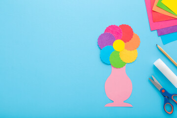 Wall Mural - Colorful flower and vase shape, scissors, glue stick, pencil and application paper on blue table background. Pastel color. Closeup. Making decoration elements. Empty place for text. Top down view.