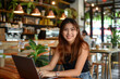© Patcharaphon - Happy young Asian woman working with laptop in coffee shop. Work from anywhere, lifestyle concept
