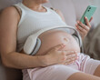 A pregnant woman turns on music for her child on a smartphone. Headphones on the tummy. 