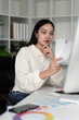 Asian woman freelance graphic designer working with color swatch samples and computer at desk in home office, young lady choosing color gamma for new design project