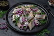 pickled herring with  red onion, capers and dill on black plate