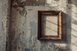 A single empty wooden picture frame hanging on a weathered white wall with sunlight shining in
