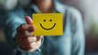 © Bnz - Close-up of a hand holding a card with a happy smiling face, symbolizing customer satisfaction and positive feedback, reflecting the concept of happy client experiences and service excellence.