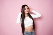 smiling attractive woman listening to music in headphones on pink background