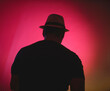 A man wearing a hat and a black shirt is standing in front of a pink background