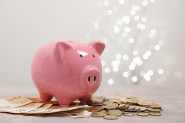 Sticker - Piggy bank with euro banknotes and coins on grey table against blurred lights, space for text