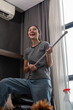 House cleaning with fun. Happy young asian housewife singing song during cleanup, using mop as guitar, enjoying domestic work. Young woman dancing and cleaning in living room