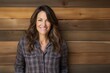 © CogniLens - Portrait of a smiling woman in her 40s wearing a comfy flannel shirt isolated on rustic wooden wall