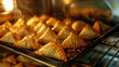 Close-up of a tray of baked samosas being pulled out of the oven, showcasing the golden crust and fragrant aroma of these healthier versions of the classic snack.