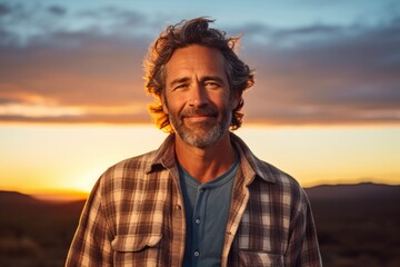 Wall Mural - Portrait of a happy man in his 50s dressed in a relaxed flannel shirt on vibrant sunset horizon