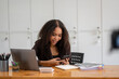 © Wasana - Cheerful African American businesswoman having a phone conversation while working on a laptop in a modern office.