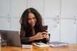 © Wasana - Cheerful African American businesswoman having a phone conversation while working on a laptop in a modern office.