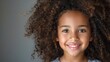 © Iuliia Metkalova - Joyful Young Girl with Curly Hair Smiling Against Grey Background. Generative ai