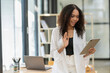 © Wasana - Smiling African American businesswoman engaging in a video call using her tablet in a modern office environment.