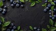 Fresh blueberries with green leaves scattered over a textured dark background with ample copy space.