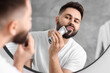 © New Africa - Handsome young man trimming beard near mirror in bathroom