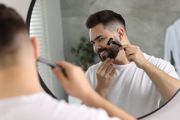 Poster - Handsome young man shaving with razor near mirror in bathroom