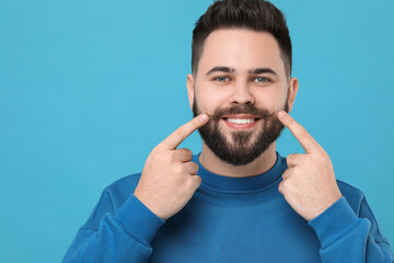 Wall Mural - Happy young man touching mustache on light blue background