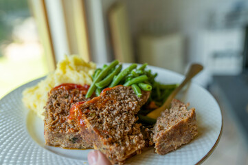 Plate with slices of fresh and homemade meatloaf. Served with mashed potatoes and green beans.