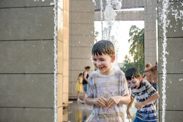 Wall Mural - Boys jumping in water fountains. Children playing with a city fountain on hot summer day. Happy friends having fun in fountain. Summer weather. Friendship, lifestyle and vacation