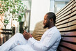 African American hipster guy in cultural and ethnic clothing dashiki chatting on smartphone outdoors, texting with friends on social networks. Millennial generation and Internet blog concept