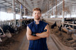 Portrait young man farmer or vet doctor on background cows in cowshed on dairy farm. Agriculture industry farming, people and animal husbandry concept