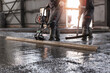 Team Workers uses vibrating machine to level cement mortar for floors. Concrete screed for buildings, construction site