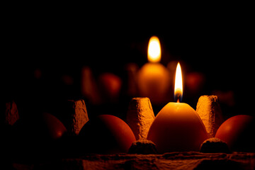 A yellow candle in the shape of an egg in the dark on a tray with chicken eggs stands near a mirror, Easter