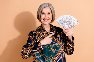 Poster - Photo of satisfied positive retired person with bob hairdo wear print blouse indicating at dollars isolated on beige color background