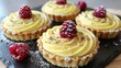  A black plate adorned with cupcakes, coated in frosting, and featuring raspberries nearby