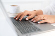 Close-up of hands typing of freelance business female casual working with laptop computer and Taking written Notes to on notebook, a coffee cup in coffee shop like,Distance job communication concept