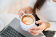 Close-up of hands Holding cup mug of Hot coffee latte wits business female casual working with laptop computer in coffee shop like the background,communication concept