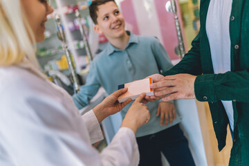 Cheerful young blonde pharmacist chemist woman giving vitamins, medicine to father and son.