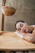 © dikushin - Vertical portrait of tranquil young woman lying on massage table with closed eyes enjoying leisure in wellness center. Happy relaxed beautiful female having rest at spa salon. Concept of body care
