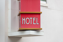 A Square Hotel Sign In The Shape Of Blocks. The Signpost Rotates On A Swivel Mechanism On A Wall. Each Block Has A Letter For The Word Hotel. The Wooden Sign Is Red With White Letters And Gold Trim.  