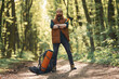 Yellow axe in hand, backpack on the ground. Bearded man is in the forest at daytime