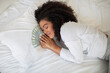 Hispanic woman is seen lounging on a bed with a fan of money spread out in front of her. She appears relaxed and content as she gazes at the cash in her hands.