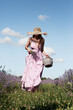 Young sexy beautiful woman in a straw hat is walking in a lavender field with a basket and a bouquet against the sky. Harvesting lavender.	